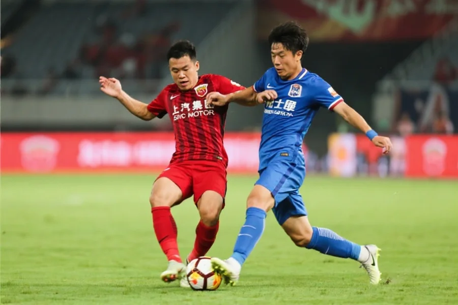 两位足球球员在中场激烈拼抢，一方身穿红色球衣，另一方身穿蓝色球衣，球场背景清晰，动作紧张